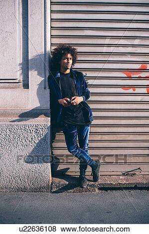 Stock Photo - Young man waiting in front of shutters. Fotosearch
