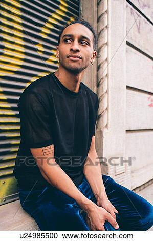 Stock Image - Young man waiting on window ledge of building. Fotosearch