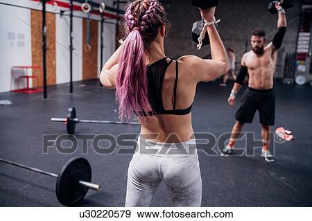 Stock Photo - Young woman and man training, lifting dumbbells in gym. Fotosearch
