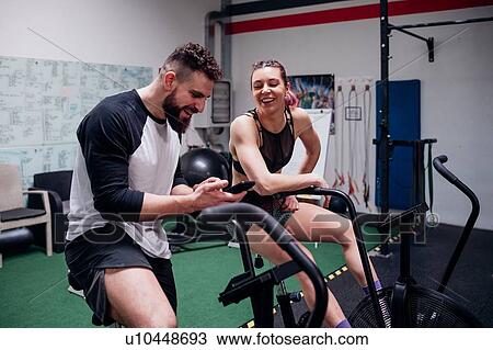 Young woman and man training together on gym exercise bikes, looking at smartphone View Large Photo Image Stock Image - Young woman and man training together on gym exercise bikes, looking at smartphone. Fotosearch