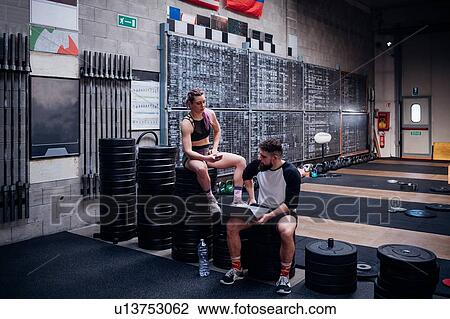 Young woman and man training together in gym, sitting on weights with smartphone and laptop View Large Photo Image Stock Image - Young woman and man training together in gym, sitting on weights with smartphone and laptop. Fotosearch