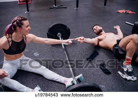 Stock Image - Young woman and man training together, touching fingers over barbell in gym. Fotosearch