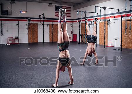 Stock Photo - Young woman and man training together, doing handstand in gym. Fotosearch