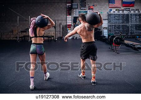 Young woman and man training together, carrying atlas ball on shoulders in gym, rear view View Large Photo Image Stock Photo - Young woman and man training together, carrying atlas ball on shoulders in gym, rear view. Fotosearch