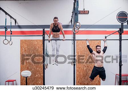Stock Photo - Young woman and man training together, on exercise bars in gym. Fotosearch