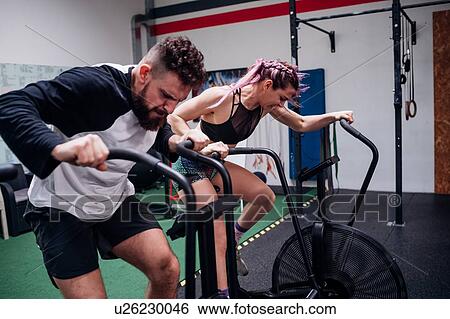 Young woman and man training together on gym exercise bikes, action View Large Photo Image Stock Photograph - Young woman and man training together on gym exercise bikes, action. Fotosearch