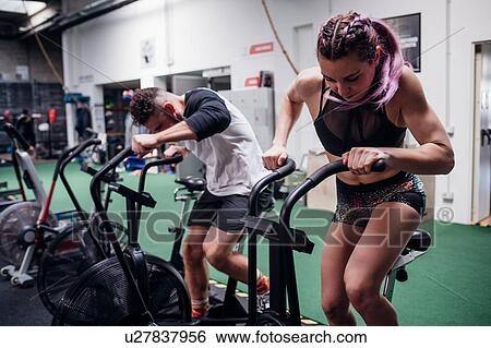 Young woman and man training together on gym exercise bikes, action View Large Photo Image Stock Photograph - Young woman and man training together on gym exercise bikes, action. Fotosearch
