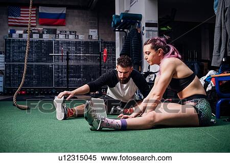 Young woman and man training together in gym, sitting on floor doing warm ups and looking at laptop View Large Photo Image Stock Photography - Young woman and man training together in gym, sitting on floor doing warm ups and looking at laptop. Fotosearch