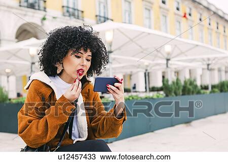 Young woman applying red lipstick using smart phone View Large Photo Image Stock Image - Young woman applying red lipstick using smart phone. Fotosearch