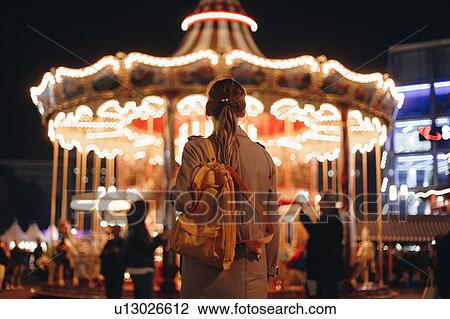 Stock Image - Young woman by carousel at night. Fotosearch