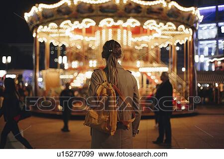 Stock Photo - Young woman by carousel at night. Fotosearch