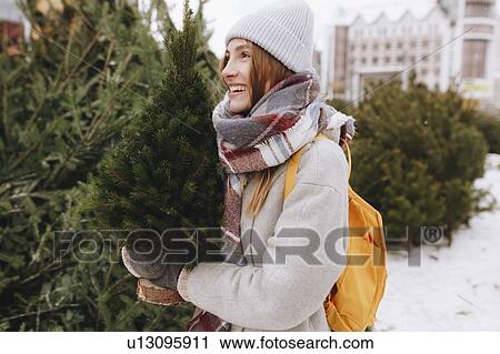 Stock Image - Young woman carrying small Christmas tree. Fotosearch