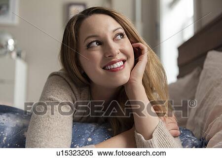 Stock Photography - Young woman day dreaming on bed. Fotosearch