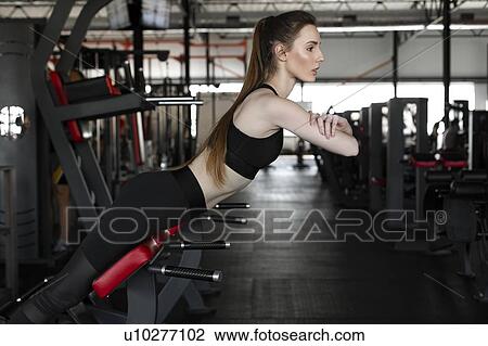 Stock Image - Young woman doing reverse sit-ups in gym. Fotosearch