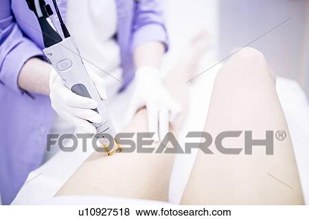 Stock Photo - Young woman getting laser hair removal treatment on leg, close-up.. Fotosearch