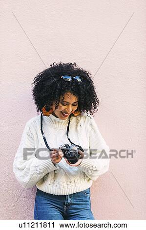 Young woman holding camera against pink wall View Large Photo Image Stock Image - Young woman holding camera against pink wall. Fotosearch