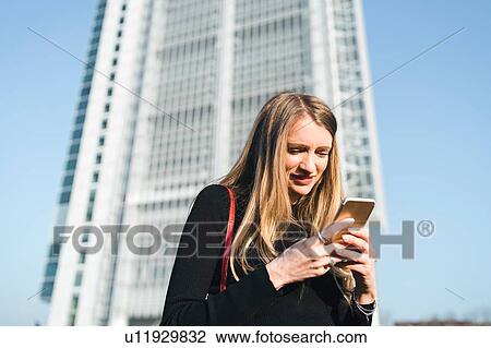 Young woman in front of skyscraper looking at smartphone, Turin, Piemonte, Italy View Large Photo Image Stock Image - Young woman in front of skyscraper looking at smartphone, Turin, Piemonte, Italy. Fotosearch