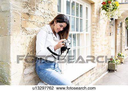Young woman leaning against street wall reviewing photos on digital camera, Cotswolds, England View Large Photo Image Stock Image - Young woman leaning against street wall reviewing photos on digital camera, Cotswolds, England. Fotosearch