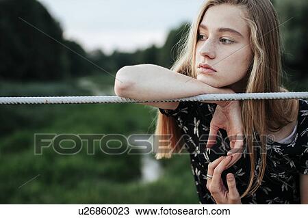 Stock Image - Young woman leaning on metal fence. Fotosearch