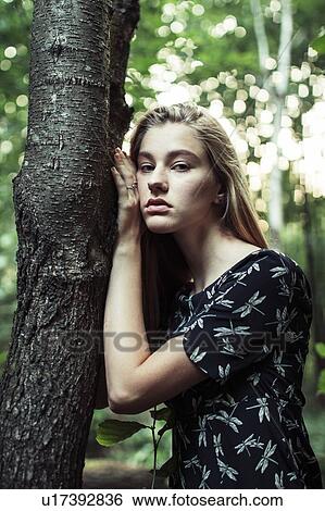 Stock Photograph - Young woman leaning on tree trunk. Fotosearch