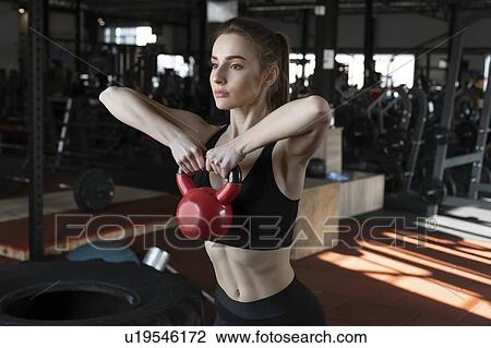 Stock Image - Young woman lifting kettlebell in gym. Fotosearch