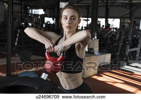 Stock Photo - Young woman lifting kettlebell in gym. Fotosearch