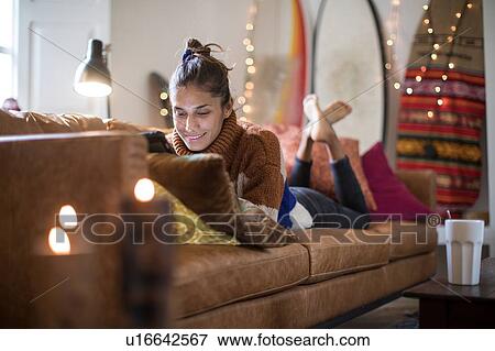 Young woman lying on living room sofa looking at laptop View Large Photo Image Stock Photo - Young woman lying on living room sofa looking at laptop. Fotosearch