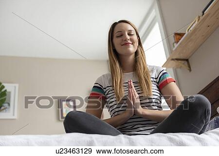 Stock Photo - Young woman meditating on bed. Fotosearch