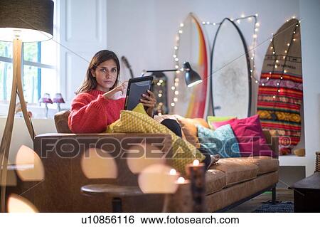 Stock Photograph - Young woman on living room sofa using digital tablet, portrait. Fotosearch