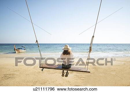 Stock Photograph - Young woman on swing at beach. Fotosearch
