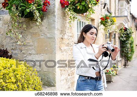 Stock Photo - Young woman on village street reviewing photos on digital camera, Cotswolds, England. Fotosearch