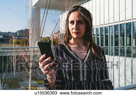 Stock Image - Young woman outside office building taking smartphone selfie, Turin, Piemonte, Italy. Fotosearch