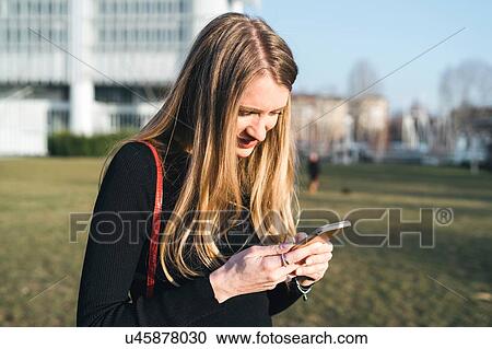 Stock Image - Young woman outside office building looking at smartphone, Turin, Piemonte, Italy. Fotosearch
