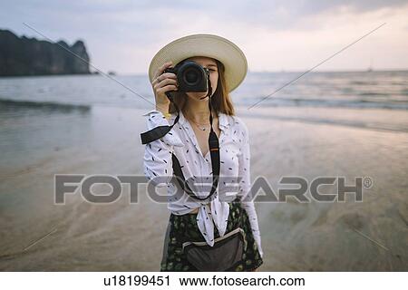 Stock Image - Young woman photographing on beach in Krabi, Thailand. Fotosearch