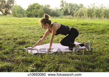 Stock Image - Young woman placing yoga mat in park. Fotosearch