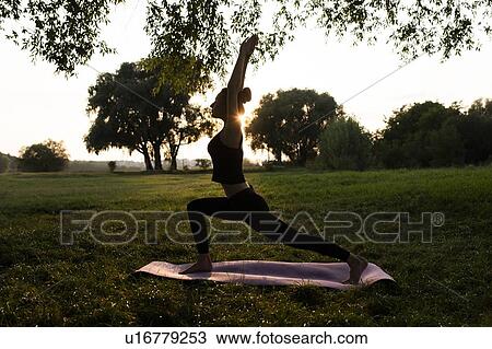 Stock Image - Young woman practicing yoga in park at sunset. Fotosearch