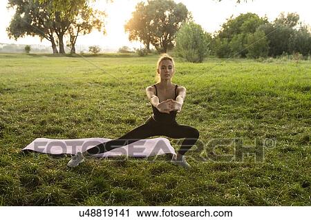 Stock Image - Young woman practicing yoga in park. Fotosearch