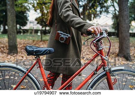 Young woman pushing bicycle in autumn park, neck down View Large Photo Image Stock Photo - Young woman pushing bicycle in autumn park, neck down. Fotosearch