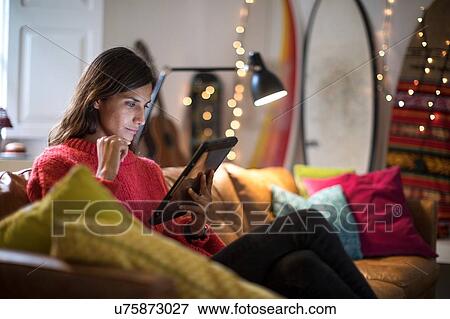 Stock Photo - Young woman relaxing on living room sofa looking at digital tablet. Fotosearch