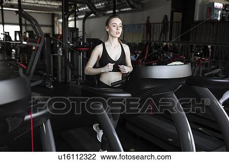 Stock Image - Young woman running on treadmill in gym. Fotosearch