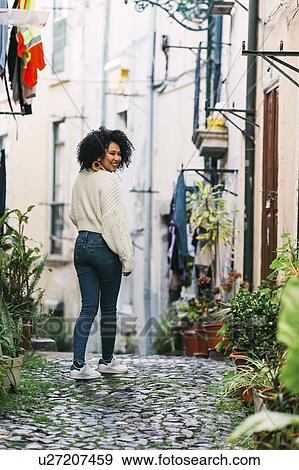 Stock Photo - Young woman smiling over shoulder in alley. Fotosearch