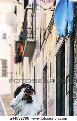 Stock Photograph - Young woman taking photograph in alley. Fotosearch
