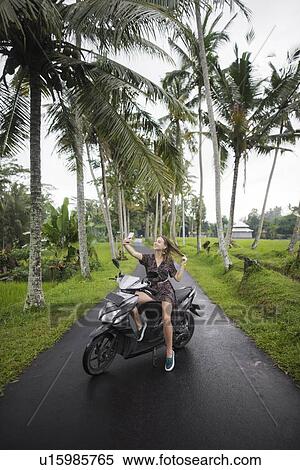 Stock Photography - Young woman taking selfie on motorcycling in Bali, Indonesia. Fotosearch