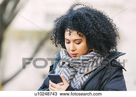 Stock Image - Young woman text messaging on smart phone. Fotosearch