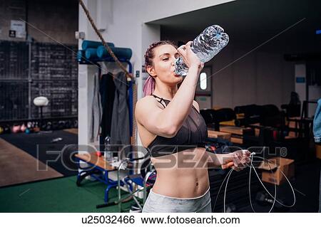 Stock Photograph - Young woman training, drinking bottled water in gym. Fotosearch