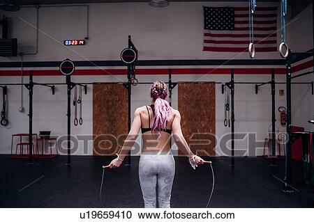 Stock Image - Young woman training, holding skipping rope in gym, rear view. Fotosearch