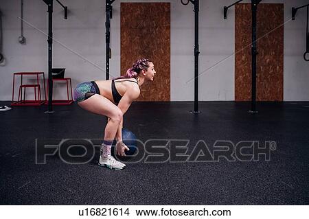 Picture - Young woman training, lifting atlas ball in gym. Fotosearch