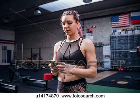 Young woman training, looking at smartphone in gym View Large Photo Image Stock Image - Young woman training, looking at smartphone in gym. Fotosearch