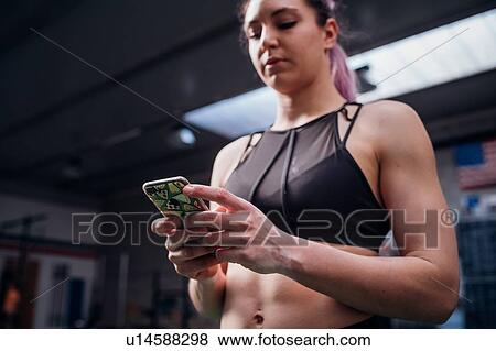Young woman training, looking at smartphone in gym, low angle view View Large Photo Image Stock Photo - Young woman training, looking at smartphone in gym, low angle view. Fotosearch