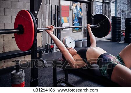 Stock Photography - Young woman training, lying on weights bench in gym preparing to lift barbell. Fotosearch